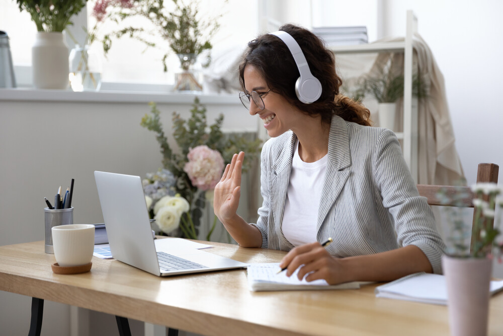 Frau winkt in den Laptop vor ihr hinein-Webinarsituation