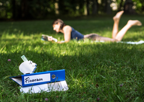 Frau liegt im Gras in der Sonne mit Ordner im Vordergrund